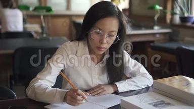 漂亮的<strong>女学生</strong>正坐在图书馆的桌子旁<strong>写字</strong>。